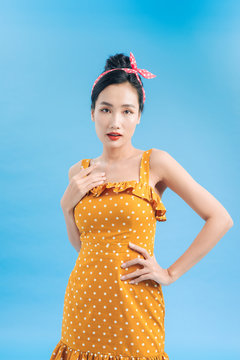 Beautiful young smiling woman wearing polka-dot dress. Model posing near blue wall in studio. Positive female