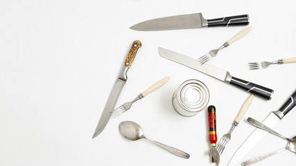kitchen utensils: opener, forks, sharp metal knives, teaspoons, tin randomly scattered on white...