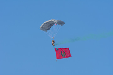 Largest Military Show Union Fortress 7 Show in UAQ with coordinated military aircrafts and parachuter with a large Umm al Quwain flag landing in the blue sky.