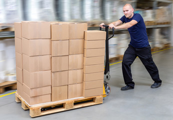 Warehouseman in storehouse fast-moving pallet with stacker. Worker in warehouse moves pallet in rack system. Caucasian labourer working with small forklift. Man rush with pallet jack.