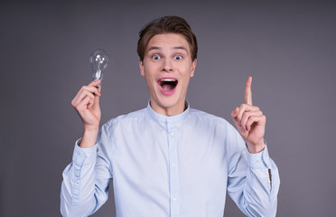 Young cheerful handsome guy with a light bulb in his hand.