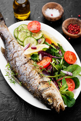 White plate of baked sea bass with fresh green salad.