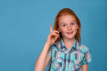 Emotional portrait of a young funny naughty girl with red hair  against  blue background