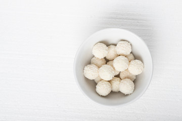 White candies with coconut, nuts and cream in a plate on a white background