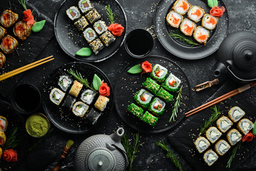 Sushi bar menu. Set of colored delicious sushi rolls on black plates. Top view.