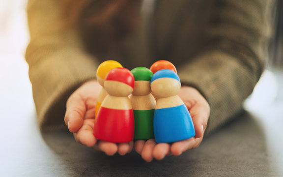 Closeup image of a woman holding a group of different colors wooden people toy in hands for diversity and business concept