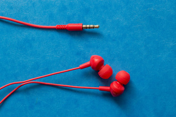 Red earphones on blue background, isolated earphones