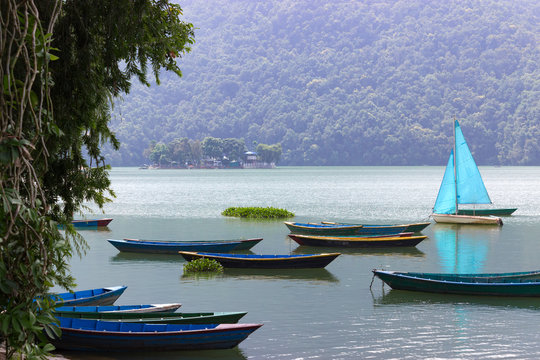 small boats of various colors, on the blue surface of the lake. Green hills and clouds on the background. Vacation in Nepal.