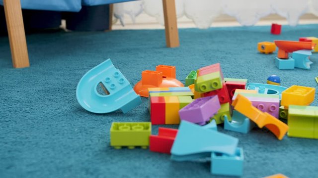 Closeup dolly footage of messy floor at childs room at house. Colorful bricks and building blocks lying on blue carpet at playroom