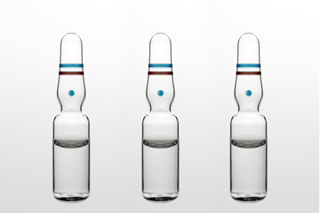 Three transparent glass ampoules with transparent liquid on white background. Close-up