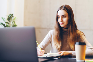 Girl studying for seminar, writing research paper, working on diploma project. Ambitious young specialist sitting at office desk, executing creative task, using laptop, Internet connection for job.