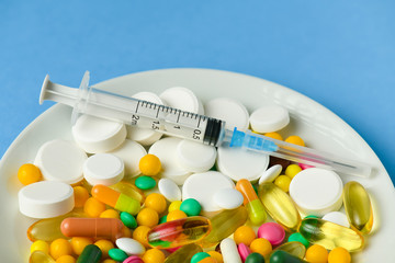 Pills, tablets, syringe, vitamins, drugs, medicine in a white dish for medical treatment. Blue background.