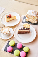 Breakfast in the cafe, morning coffee. Cappuccino and lots of desserts on the table. Napoleon, chocolate cake, cheesecake and macaroons.