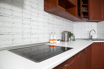 Interior of domestic kitchen with cooktop electric touch stove and long white tabletop with sink