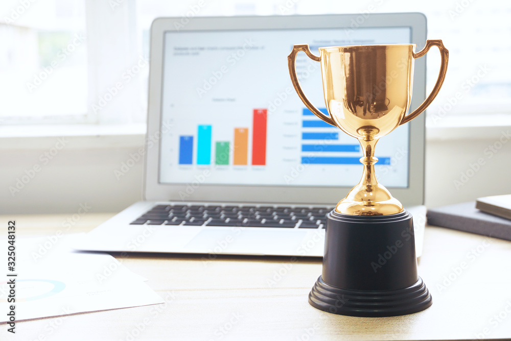 Wall mural gold trophy with background laptop computer on the working table near the window.