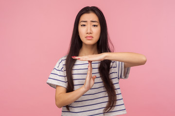 Fototapeta premium Stop, enough, I need break. Portrait of exhausted girl with long hair in t-shirt showing time-out gesture and looking imploringly, asking for pause. indoor studio shot isolated on pink background