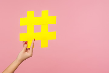 Closeup of hand holding large yellow paper hashtag symbol next to copy space, hash sign of famous...