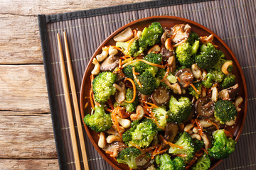 Serving of fried broccoli with shiitake, carrots and cashew nuts close-up in a plate. Horizontal top view
