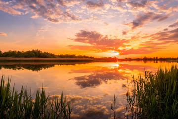 Scenic view of beautiful sunset or sunrise above the pond or lake at spring or early summer evening...