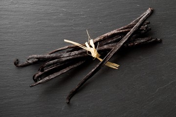 Bundle of tied, dried bourbon vanilla beans or pods on black stone board flat lay top view