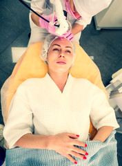 Young woman having face polishing procedure in beauty salon. Doctor cosmetologist makes the procedure using professional laser system to a woman patient. Laser resurfacing and face treatment