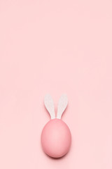 Fototapeta Huevo de pascua de color rosa pastel con orejas de conejo de color blanco sobre fondo rosa pastel vertical. obraz