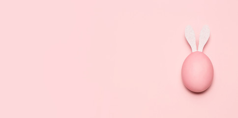 Huevo de pascua de color rosa pastel con orejas de conejo de color blanco sobre fondo rosa pastel horizontal. - obrazy, fototapety, plakaty