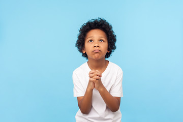 Please, I'm begging. Portrait of upset little boy praying to god with hands held together, apologizing for bad behavior, looking up with imploring eyes. indoor studio shot isolated on blue background - obrazy, fototapety, plakaty