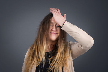 Exasperate female keeps hands on temples, feels strong headache, closes eyes with pain, need healthy sleep, being overworked, fatigue and tired. Europea woman being ill, isolated over gray background