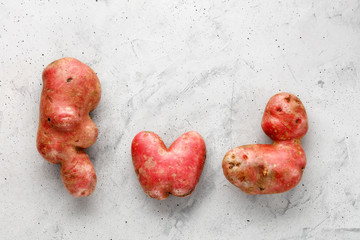 Ugly potato in the heart shape and letter shape on a background of gray concrete. Vegetables or...