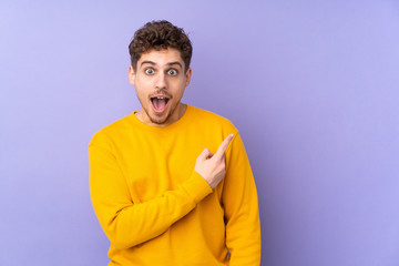 Caucasian man isolated on purple background surprised and pointing side