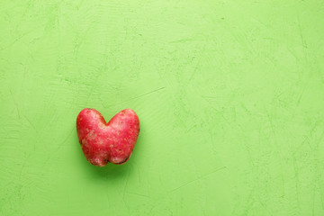 Ugly potato in the heart shape on a green concrete plaster background. Vegetable or food waste concept. Top view, close-up.