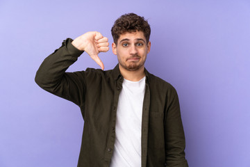 Caucasian man isolated on purple background showing thumb down with negative expression