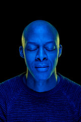 Black man with eyes closed. Studio photo with blue light isolated on black background. Concentration or peace concept. Vertical