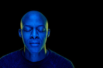 Black man with eyes closed. Studio photo with blue light isolated on black background. Concentration or peace concept. Horizontal with copyspace