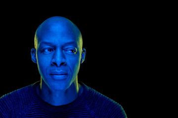 Studio photo with blue light of a black man looking sideways. Isolated on black background. Horizontal with copyspace