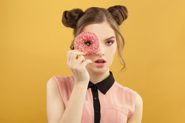 Fashionable woman holding donut on vivid yellow background, diet concept