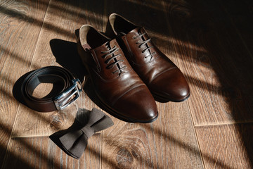 Close up of brown male shoes, bowtie and belt on wood floor background, copy space. Modern man accessories. Wedding details