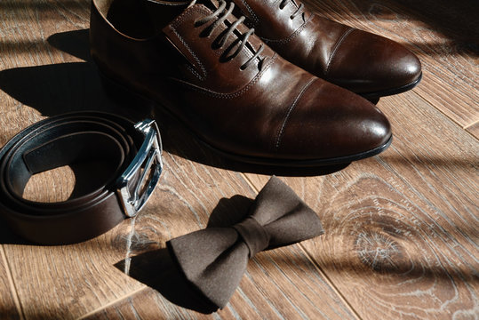 Close up of brown male shoes, bowtie and belt on wood floor background, copy space. Modern man accessories. Wedding details