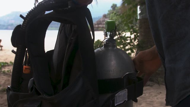 Man on an exotic beach fixing BCD (buoyancy control device) on a gas bottle, Comoros islands, Moheli
