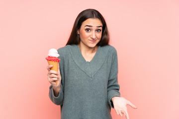 Young woman holding a cornet ice cream isolated on pink background making doubts gesture while lifting the shoulders