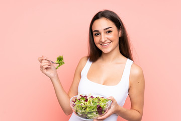 Young caucasian woman holding a salad isolated on pink background