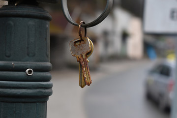 Bunch of old, rusty metal keys in key ring hanging on hook. Blurry town background.