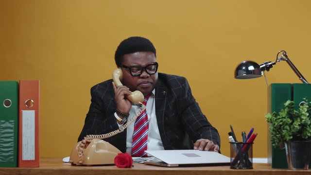 Black businessman boss talks telephone call conversation with employee or partner closing his laptop working at the office corporation.