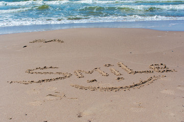 Drawn smile symbol and word smile written in beach sand with blue sea and waves in background