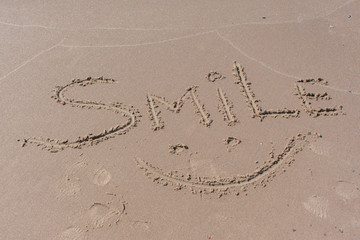 Drawn smile symbol and word smile written in beach sand with blue sea and waves in background