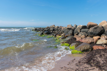 Landscape of beach covered in stones. Blue water. Cloudy sky background.