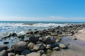 Fototapeta na wymiar Landscape of beach covered in stones. Blue water. Cloudy sky background.