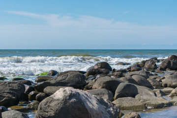 Fototapeta premium Landscape of beach covered in stones. Blue water. Cloudy sky background.