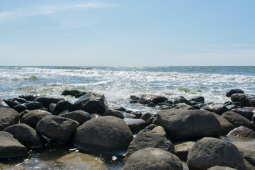 Landscape of beach covered in stones. Blue water. Cloudy sky background.